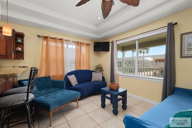 tiled living room with a tray ceiling and ceiling fan