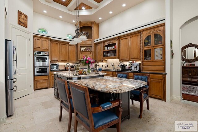 kitchen with a high ceiling, a center island with sink, dark stone countertops, a kitchen bar, and stainless steel appliances