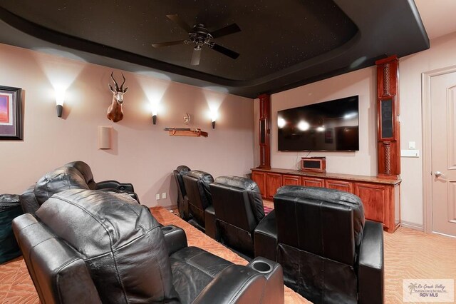 home theater with ceiling fan, light colored carpet, and a tray ceiling