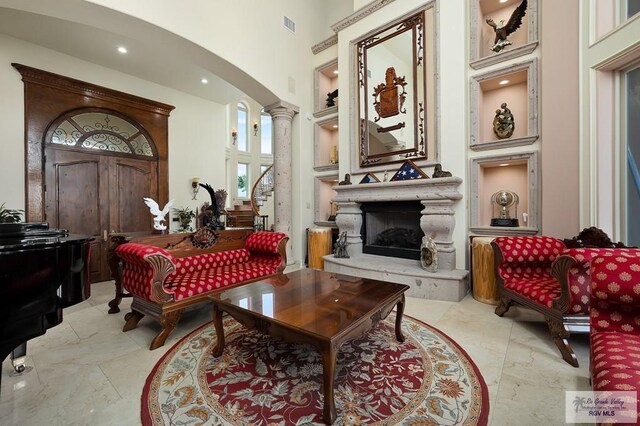 sitting room featuring built in shelves, a towering ceiling, and ornate columns