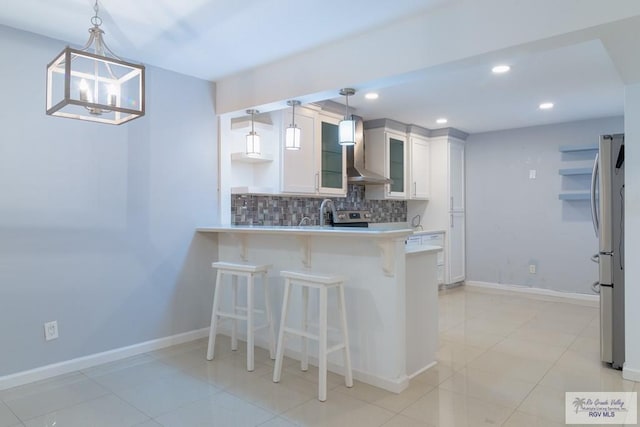 kitchen with white cabinetry, wall chimney range hood, tasteful backsplash, decorative light fixtures, and a breakfast bar