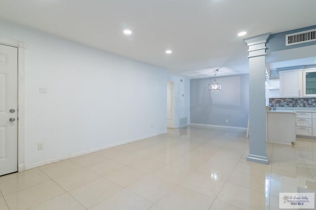 unfurnished room featuring decorative columns, sink, and light tile patterned flooring