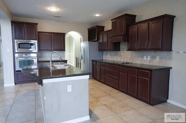 kitchen with backsplash, a center island with sink, sink, appliances with stainless steel finishes, and light tile patterned flooring