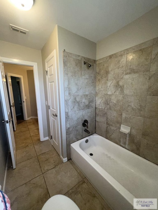 bathroom featuring tile patterned flooring, toilet, and tiled shower / bath