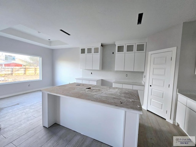 kitchen with a raised ceiling, a center island, white cabinets, and dark hardwood / wood-style flooring