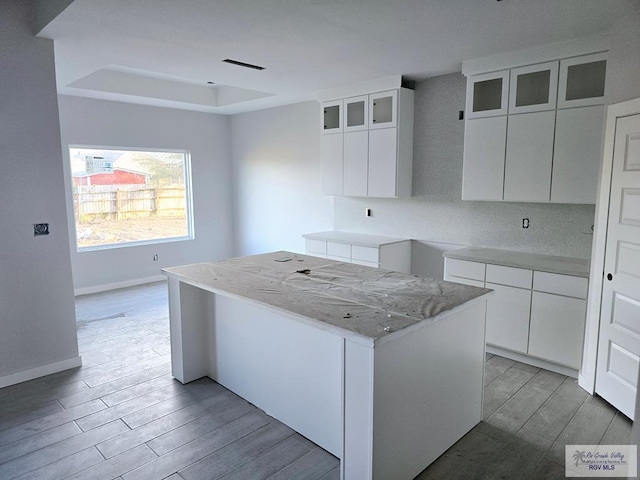 kitchen featuring white cabinetry, a center island, light wood-type flooring, a raised ceiling, and backsplash