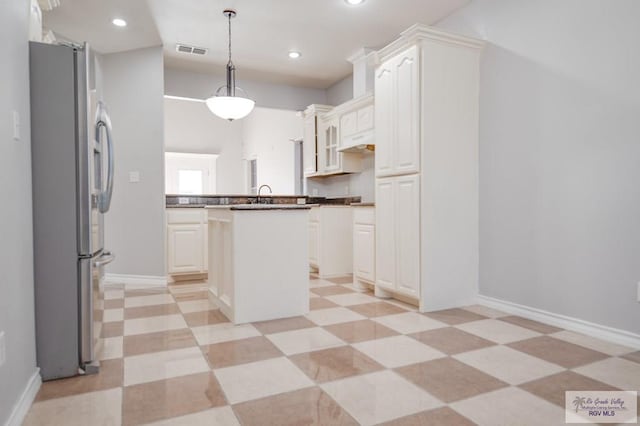 kitchen with pendant lighting, sink, a kitchen island, white cabinetry, and stainless steel refrigerator