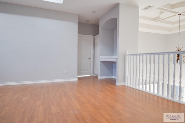 unfurnished room featuring a chandelier, a skylight, and light hardwood / wood-style flooring