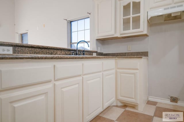 6724 Pino Verde Dr, Brownsville, TX 78526 - kitchen with white cabinets, under cabinet range hood, a sink, dark stone counters, and glass insert cabinets