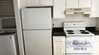 kitchen with dark countertops, white cabinetry, under cabinet range hood, and white appliances