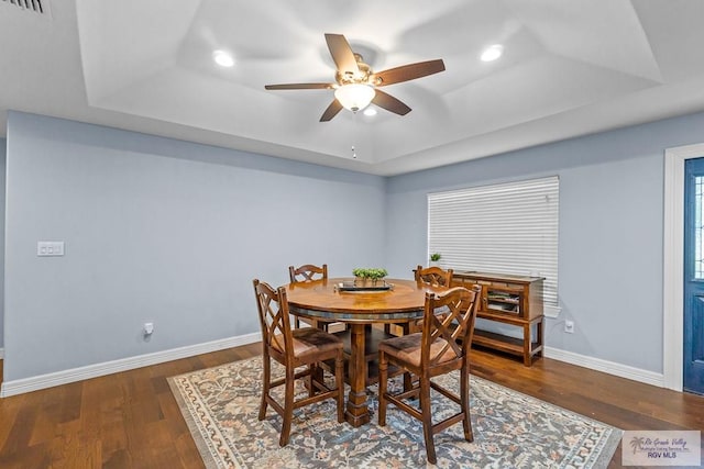 dining room with dark hardwood / wood-style floors, ceiling fan, and a tray ceiling