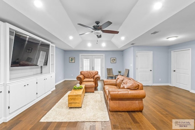 living room with french doors, ceiling fan, a raised ceiling, and dark wood-type flooring