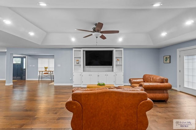 living room with hardwood / wood-style flooring, a raised ceiling, and ceiling fan