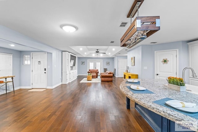 interior space featuring blue cabinetry, a tray ceiling, dark hardwood / wood-style flooring, ceiling fan, and light stone countertops