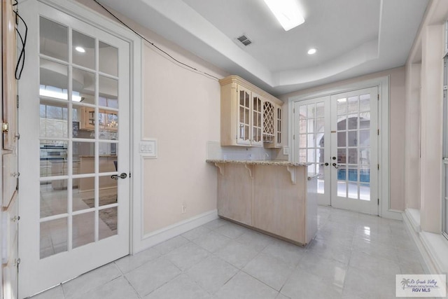 kitchen featuring french doors, light tile patterned floors, a tray ceiling, a kitchen bar, and kitchen peninsula