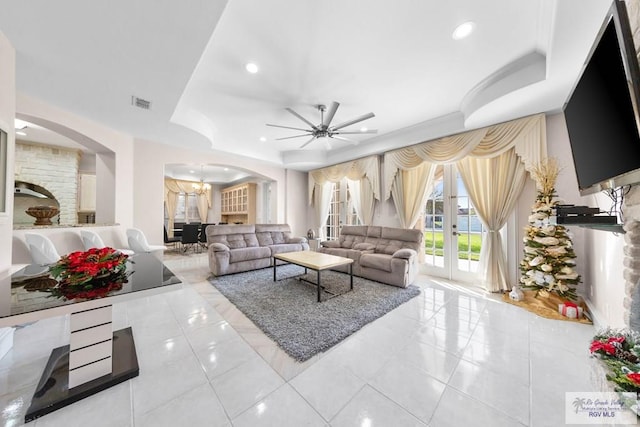 tiled living room featuring french doors, ceiling fan with notable chandelier, and a raised ceiling