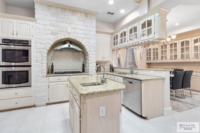 kitchen with backsplash, light stone countertops, stainless steel appliances, and a kitchen island with sink