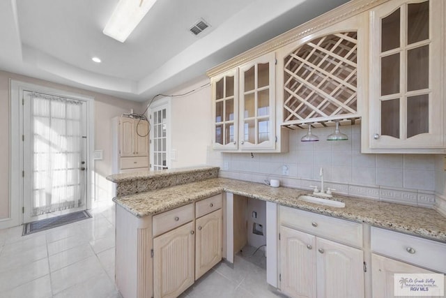 kitchen with light stone countertops, sink, kitchen peninsula, a tray ceiling, and light tile patterned floors