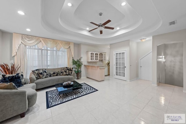 tiled living room with ceiling fan and a tray ceiling