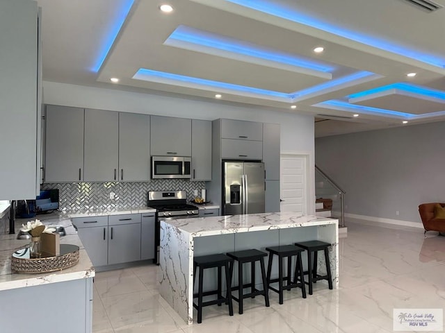 kitchen with light stone countertops, gray cabinetry, a breakfast bar, stainless steel appliances, and a kitchen island