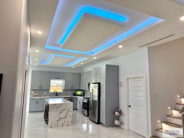 kitchen with appliances with stainless steel finishes, a breakfast bar, a tray ceiling, sink, and a center island