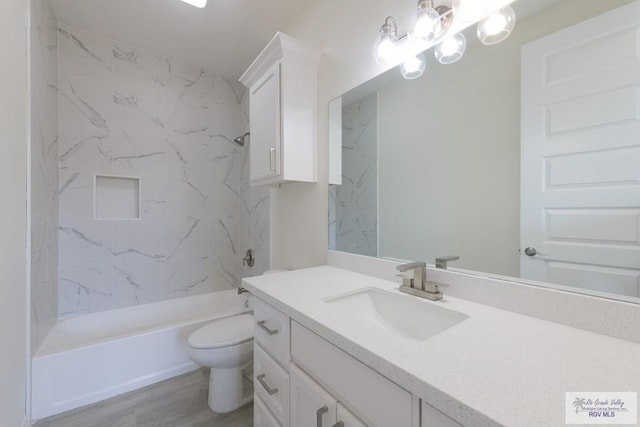 full bathroom featuring hardwood / wood-style floors, vanity, tiled shower / bath combo, and toilet