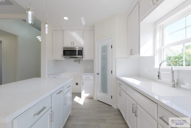 kitchen with light stone countertops, sink, white cabinets, and pendant lighting