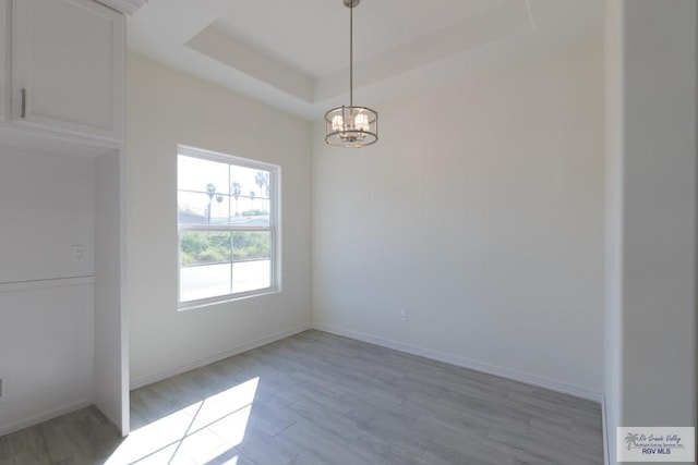 spare room with a raised ceiling, light wood-type flooring, and an inviting chandelier