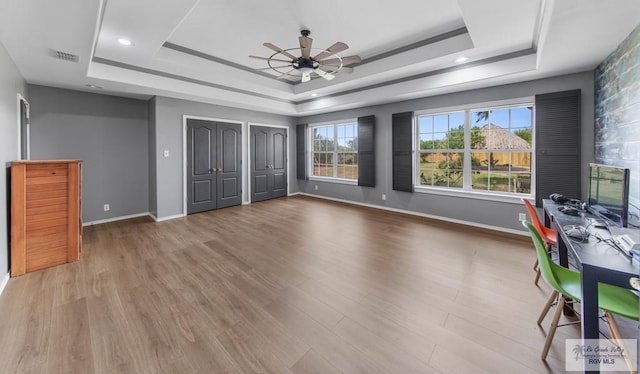 unfurnished bedroom with a tray ceiling, ceiling fan, two closets, and light wood-type flooring