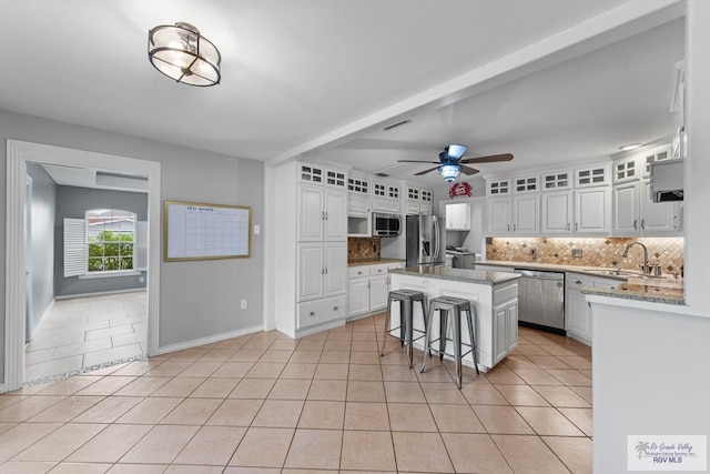 kitchen with appliances with stainless steel finishes, a kitchen breakfast bar, a kitchen island, sink, and white cabinetry