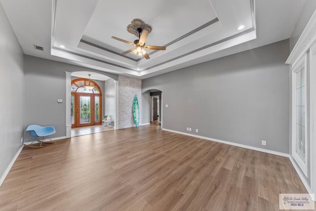 unfurnished living room featuring a raised ceiling, ceiling fan, and light hardwood / wood-style flooring