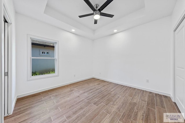 empty room featuring a raised ceiling, ceiling fan, and light hardwood / wood-style flooring