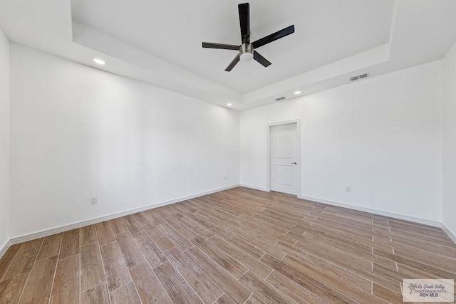 unfurnished room with ceiling fan, a raised ceiling, and light wood-type flooring