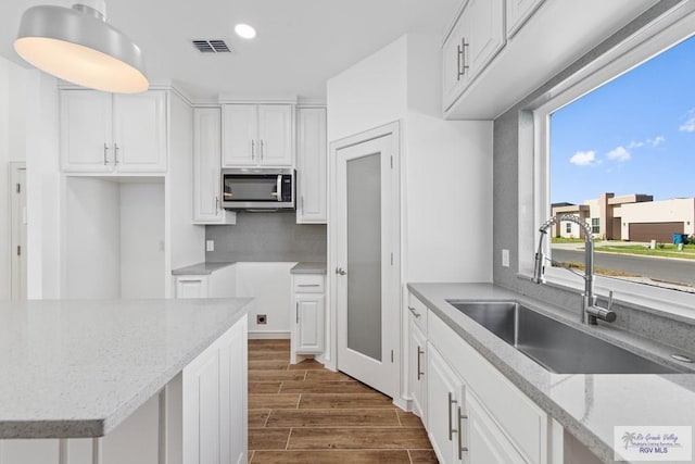 kitchen with light stone counters, white cabinetry, dark wood-type flooring, and sink