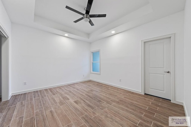 empty room with a raised ceiling, ceiling fan, and wood-type flooring