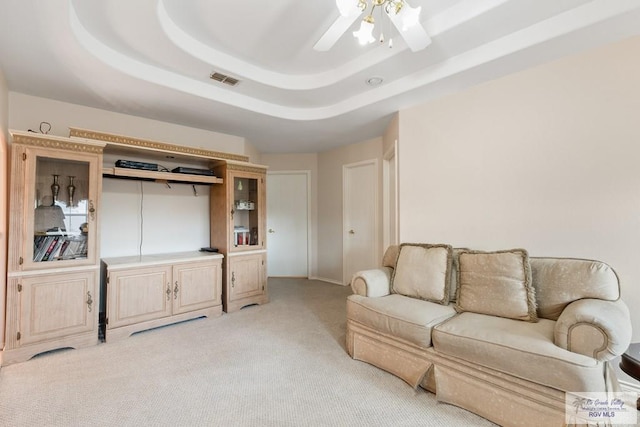 living room featuring ceiling fan, light carpet, and a tray ceiling