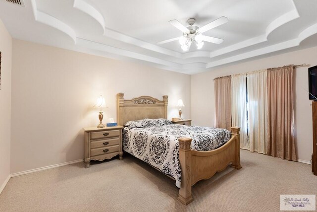 bedroom featuring ceiling fan, light colored carpet, and a tray ceiling