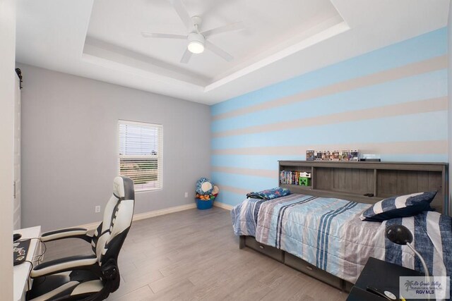 bedroom with hardwood / wood-style flooring, ceiling fan, and a raised ceiling