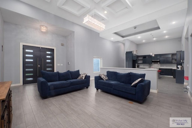 living room featuring coffered ceiling, a chandelier, a towering ceiling, and light hardwood / wood-style flooring