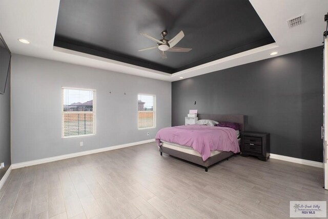 bedroom featuring a raised ceiling, ceiling fan, and light hardwood / wood-style flooring