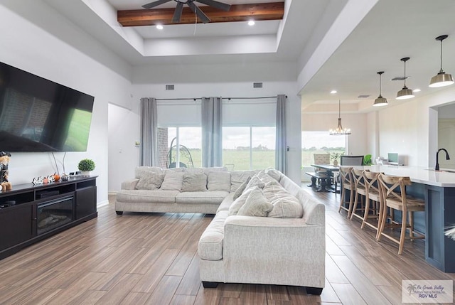 living room featuring beam ceiling, ceiling fan with notable chandelier, light hardwood / wood-style flooring, and a wealth of natural light