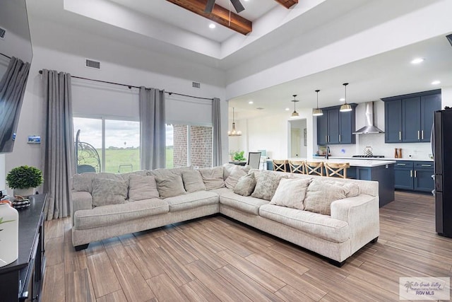 living room with ceiling fan, sink, beam ceiling, light hardwood / wood-style flooring, and a high ceiling