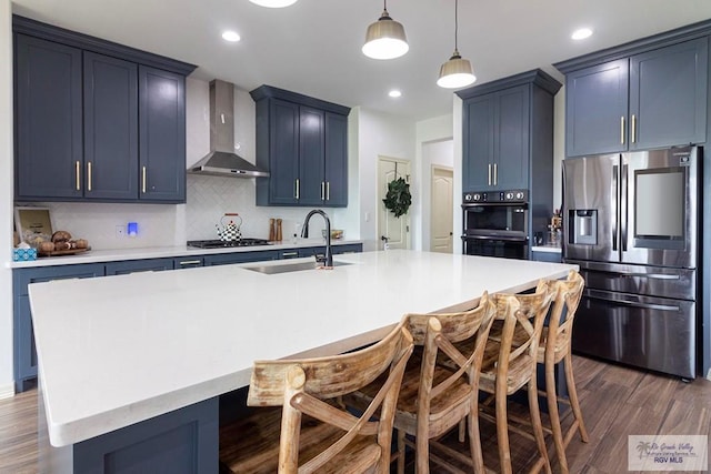 kitchen featuring a kitchen bar, appliances with stainless steel finishes, wall chimney exhaust hood, a kitchen island with sink, and dark hardwood / wood-style floors