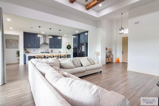 living room featuring a high ceiling, an inviting chandelier, sink, light wood-type flooring, and beamed ceiling