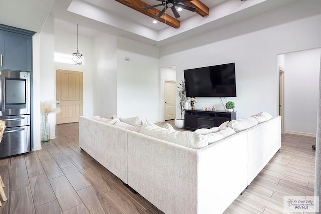 living room with a high ceiling, hardwood / wood-style flooring, ceiling fan, and beam ceiling