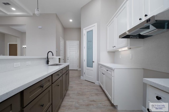 3729 Marco Ave, Harlingen, TX 78550 - kitchen with under cabinet range hood, a sink, light wood-style flooring, white cabinetry, and light stone countertops