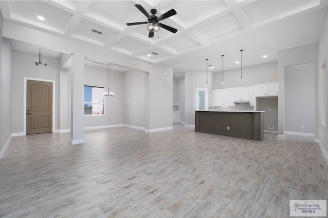 unfurnished living room with beam ceiling, ceiling fan with notable chandelier, light hardwood / wood-style floors, and coffered ceiling