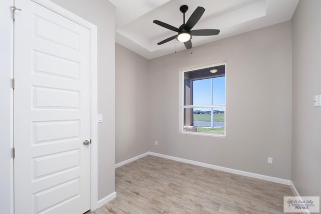 spare room featuring a tray ceiling, ceiling fan, and light wood-type flooring