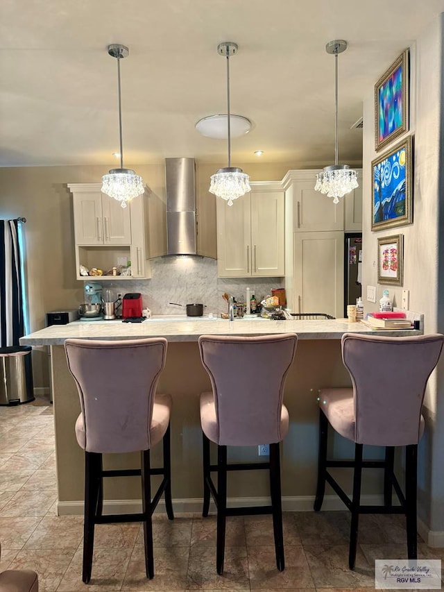 kitchen with wall chimney exhaust hood, a breakfast bar area, decorative light fixtures, and a chandelier