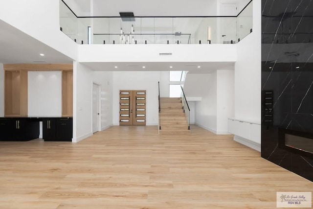 unfurnished living room with stairs, light wood finished floors, and a high ceiling